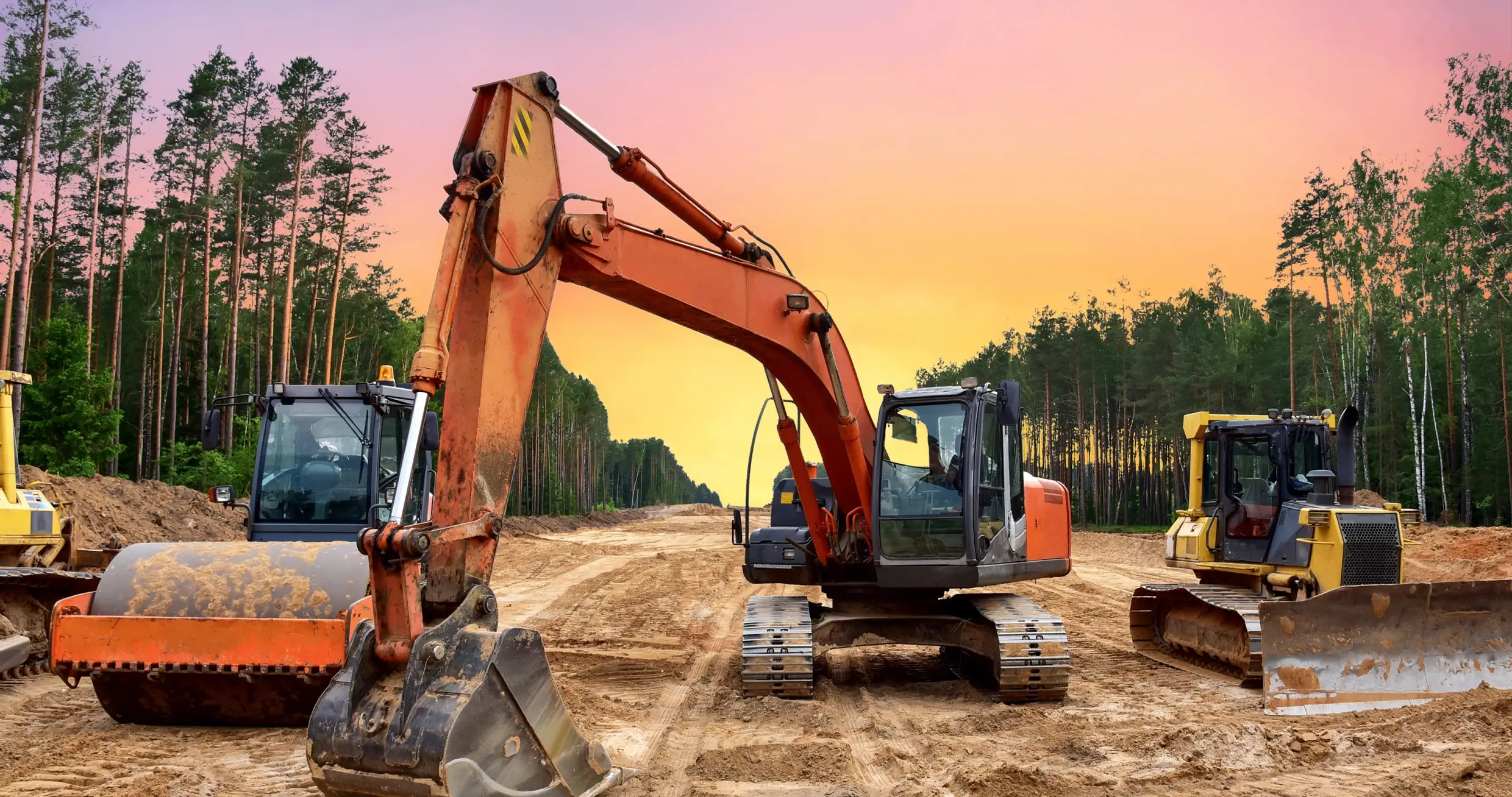 Construction vehicles on a dirt road at sunset.