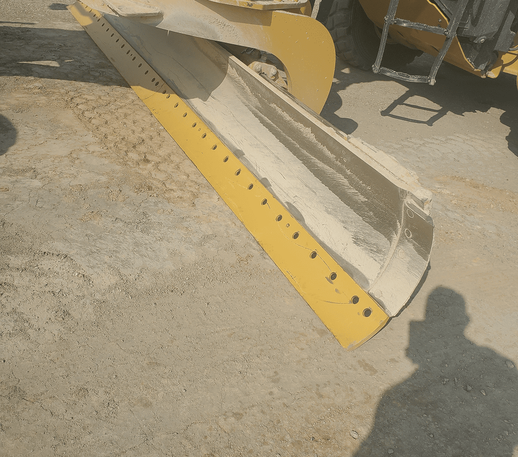 Yellow bulldozer blade on dusty ground.
