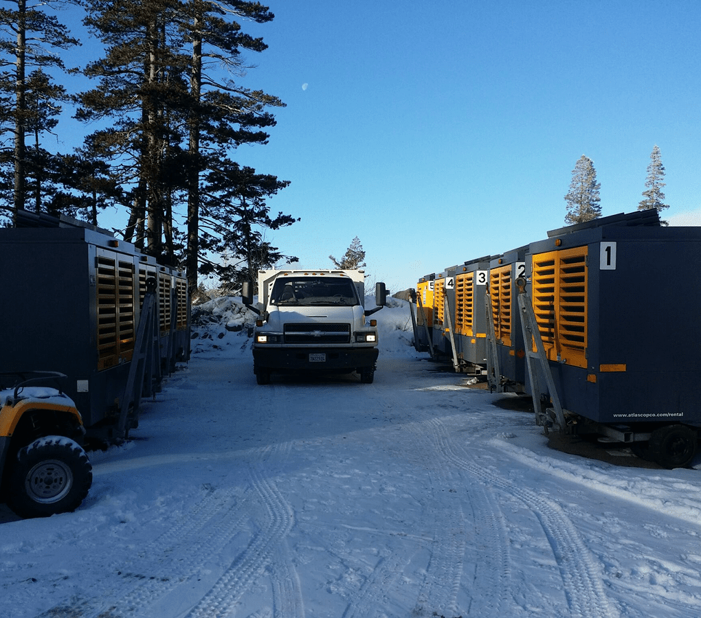 Truck parked between industrial equipment in snow.